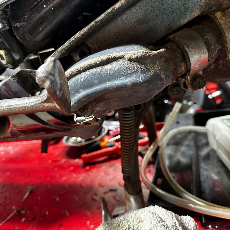 Rusty motorcycle kickstand on a red mechanic's lift.