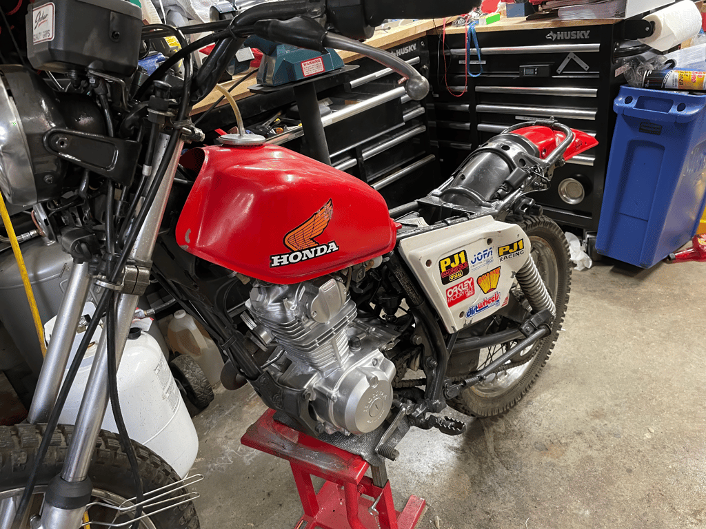 1979 Honda XL125s: red Honda fuel tank and engine in the shop